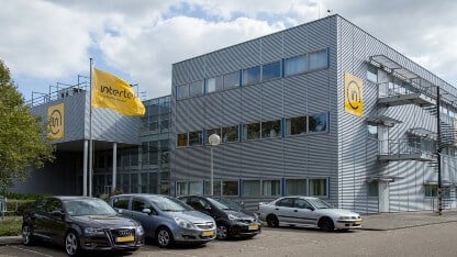 Exterior view of the multi-story Intertek Geleen polymer testing laboratory which has grey walls with yellow signage and flags